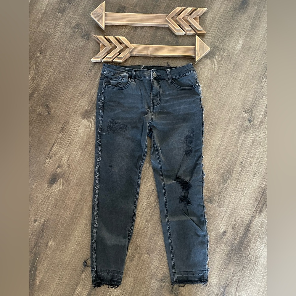 Faded black distressed, ripped jeans with frayed side hem and frayed ankle.